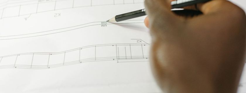 Une main tient un crayon au-dessus d’un plan technique déplié